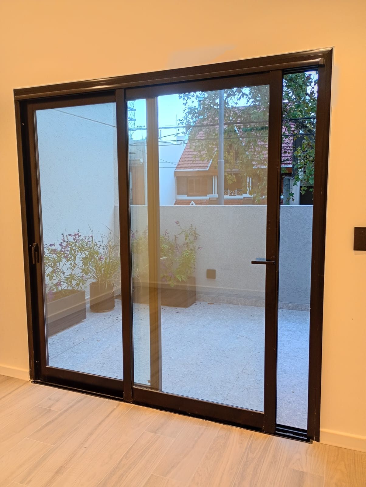 Corrediza de aluminio oscuro que da a una terraza con plantas