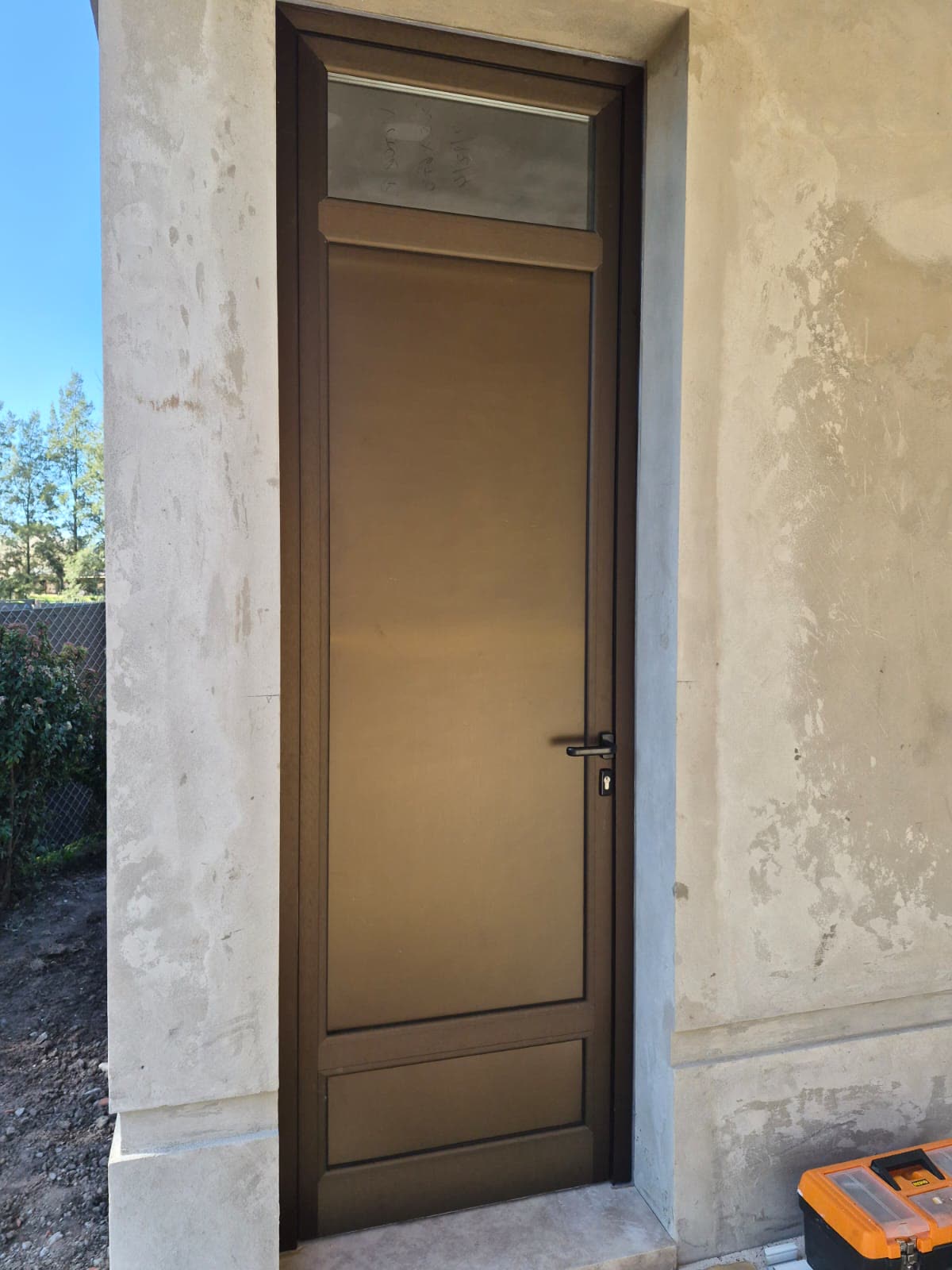 Puerta de aluminio color bronce con banderola de vidrio en una fachada
